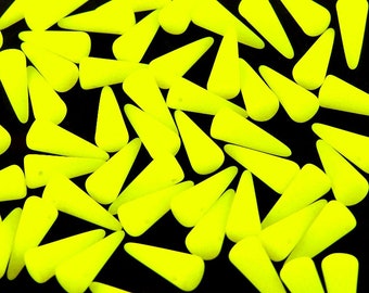 May include: A group of bright yellow glass beads in the shape of a teardrop. The beads are scattered on a black surface.