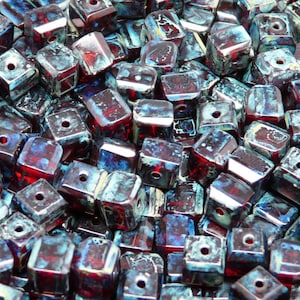 Może przedstawiać: Duża sterta ciemnoczerwonych i niebieskich kwadratowych koralików szklanych z otworem w środku każdego koralika.