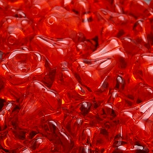 Puede incluir: Primer plano de un montón de cuentas de vidrio rojas con forma de campana. Las cuentas son translúcidas y tienen un acabado brillante.