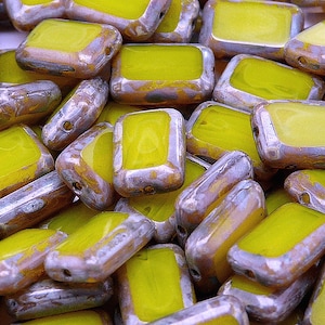 May include: A close-up of a pile of yellow glass beads with a silver metallic finish. The beads are rectangular in shape and have a slightly irregular texture.