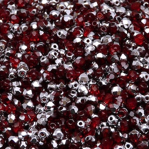 Puede incluir: Una imagen de primer plano de una mezcla de cuentas de vidrio facetadas rojas y plateadas. Las cuentas son pequeñas y tienen un acabado brillante.