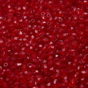 May include: A close-up view of a large quantity of small, red, faceted glass beads. The beads are arranged in a random pattern, creating a textured surface.