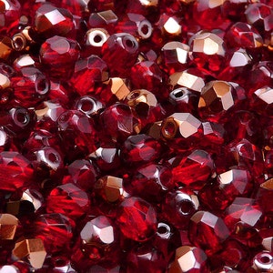 Puede incluir: Una vista de cerca de un montón de cuentas de vidrio rojas con un acabado facetado. Las cuentas tienen un brillo metálico y son perfectas para la elaboración de joyas.