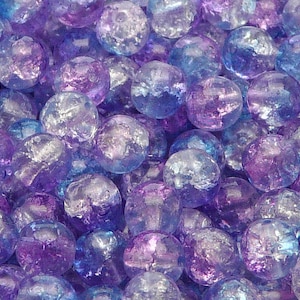 Könnte beinhalten: Nahaufnahme eines Stapels irisierender Glasperlen in Blautönen und Violett. Die Perlen sind rund und haben eine leicht strukturierte Oberfläche.