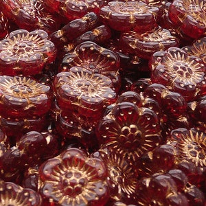 Op de afbeelding: Close-up van een verzameling donkerrode, bloemvormige kralen. Elke kraal heeft een gedetailleerd bloemenontwerp met goudkleurige accenten. De kralen zijn bij elkaar gegroepeerd, waardoor een textuurrijke en visueel rijke weergave ontstaat, ideaal voor het maken van sieraden.