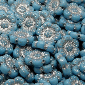 May include: A close-up of a pile of light blue glass flower beads with silver accents. The beads are small and have a delicate, feminine look.