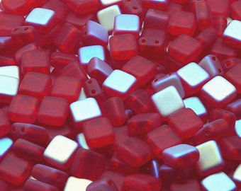 May include: A close-up of a pile of small, square, red glass beads with iridescent shimmer. The beads have two holes each.