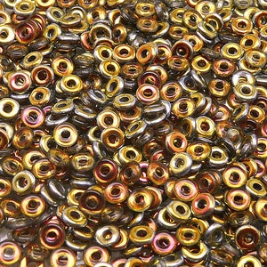 Könnte beinhalten: Nahaufnahme einer großen Menge kleiner, runder, goldener und silberner Perlen. Die Perlen haben ein Loch in der Mitte und sind in einem zufälligen Muster angeordnet.