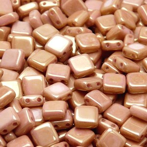 May include: A close-up of a pile of small, square, iridescent peach-colored glass beads.