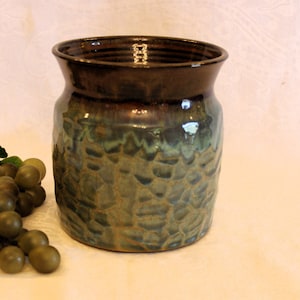 May include: A ceramic vase with a brown rim and a green and brown glaze. The vase has a textured surface and is about 6 inches tall.