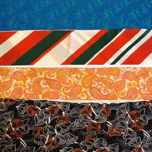 May include: Four different fabric swatches with various patterns. The top swatch is a solid blue with a small floral pattern. The second swatch is a red and white striped pattern with green stripes. The third swatch is a paisley pattern in orange, pink, and white. The bottom swatch is a black fabric with a white and orange floral pattern.