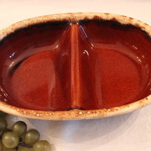 May include: A divided serving dish made of brown and white ceramic with a speckled glaze. The dish has two oval-shaped sections.