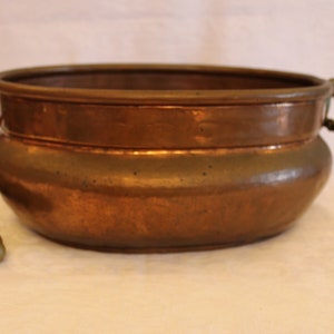 May include: A large, round copper planter with two brass handles. The planter has a hammered finish and is in good condition.