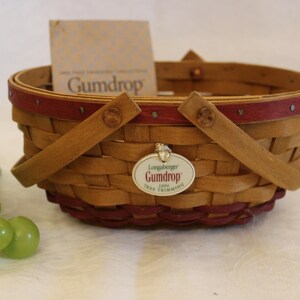 May include: A small, woven basket with red trim and a Longaberger Gumdrop 2003 Tree Trimming tag. The basket has two handles and is made of natural wood.