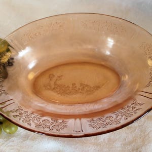 May include: A vintage pink glass serving bowl with a floral design. The bowl is oval shaped and has a raised rim.