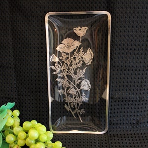May include: A clear glass serving tray with a silver floral design. The tray has a gold rim and is rectangular in shape.