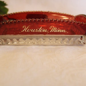May include: A red glass dish with a clear glass base. The dish has a beaded edge and the words "Houston, Minn." are etched on the front.
