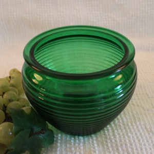 May include: A green glass jar with a ribbed design. The jar is empty and has a wide mouth.