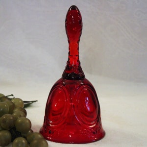 May include: A red glass bell with a decorative design. The bell has a rounded base and a tall, slender handle.