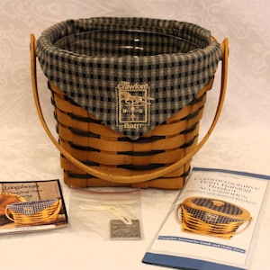 May include: A brown and black woven basket with a black and white checkered fabric liner. The basket has a leather handle and a logo that says "The Crawford Basket Co."