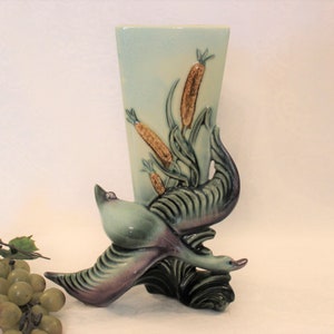 May include: A vintage ceramic vase with a green and blue glaze features a stylized flying duck design. The vase has a rectangular shape and is decorated with brown and yellow reeds.