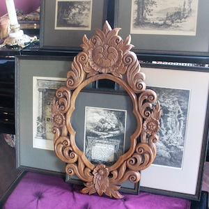 May include: A large, intricately carved wooden frame with a decorative floral design. The frame is empty, but there are several framed prints behind it.