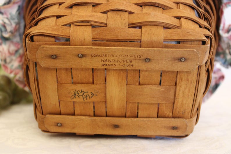 May include: A close-up of the bottom of a brown woven basket. The basket is labeled "Longaberger Basket" and "Handwoven,  Ohio, USA". The basket is signed "K.E.B. 1993".
