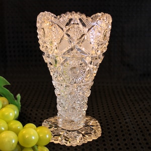 May include: A clear glass vase with a cut glass design. The vase has a wide mouth and a narrow base.