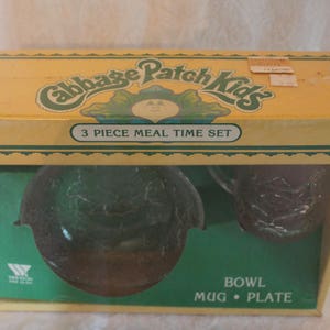 May include: A yellow box with a green and white Cabbage Patch Kids logo. The box contains a 3 piece meal time set, including a bowl, mug, and plate. The set is made of clear glass with a green design.