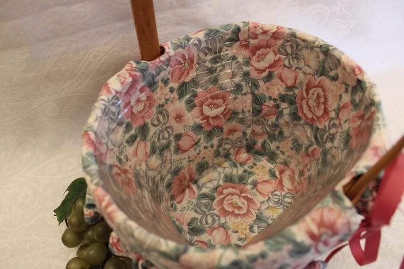May include: A floral patterned fabric basket with wooden handles. The basket is empty and ready to be filled with items.