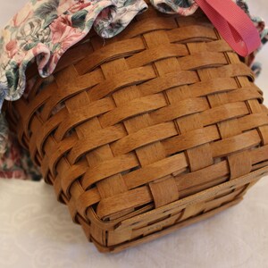 May include: A brown woven basket with a floral fabric lining and a pink ribbon. The basket is made of natural wood and has a square shape.