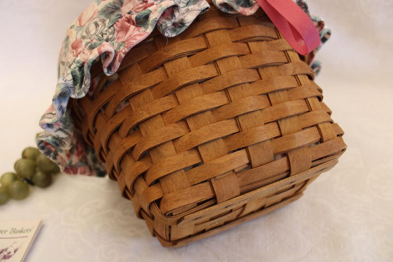 May include: A brown woven basket with a floral fabric lining and a pink ribbon. The basket is made of natural wood and has a square shape.