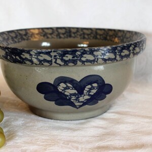 May include: A blue and white ceramic mixing bowl with a heart design. The bowl has a speckled glaze and a blue rim.
