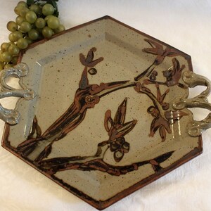 May include: A hexagonal ceramic serving tray with two handles. The tray is decorated with a brown and white floral design.