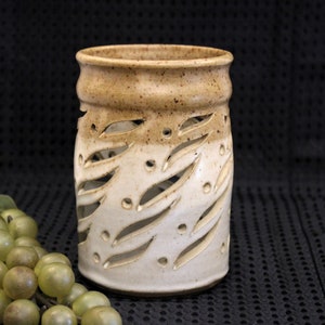 May include: A white ceramic candle holder with a brown glaze on the top. The holder has a cut-out design of leaves and dots.