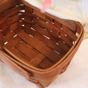 May include: A brown woven basket with a handle. The basket is empty and has a light brown wood finish.