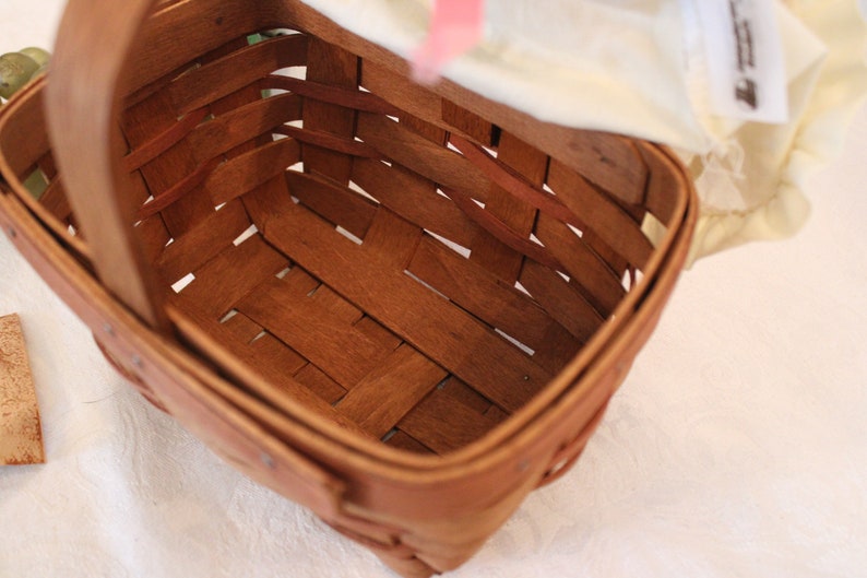 May include: A brown woven basket with a handle. The basket is empty and has a light brown wood finish.