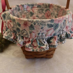 May include: A pink and green floral patterned basket with a ruffled edge and red ribbon handles.