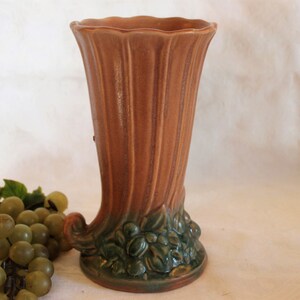 May include: A brown ceramic vase with a green leafy design at the base. The vase has a fluted design and a wide opening.