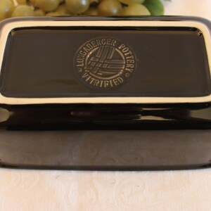 K&ouml;nnte beinhalten: Schwarze rechteckige Keramik-Backform mit wei&szlig;em Rand. Der Boden der Form tr&auml;gt ein kreisf&ouml;rmiges Logo mit der Aufschrift "Locgaderger Pottery Vitrified".