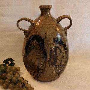 May include: A brown ceramic vase with two handles and black abstract designs. The vase is sitting on a white surface.