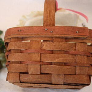 May include: A brown woven basket with a wooden handle. The basket is empty and has a light brown stain on the bottom.
