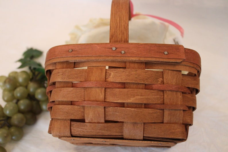 May include: A brown woven basket with a wooden handle. The basket is empty and has a light brown stain on the bottom.