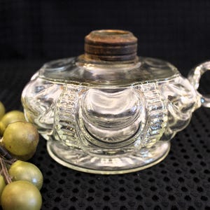 May include: A clear glass oil lamp with a decorative, scalloped design. The lamp has a metal top and a handle.