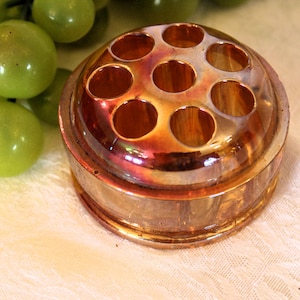 May include: A vintage iridescent glass flower frog with seven holes for arranging flowers. The frog is a light amber color with a gold sheen.