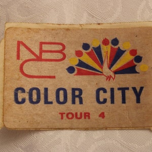 May include: A vintage NBC Color City Tour 4 sticker with a peacock design in red, yellow, and blue. The sticker is on a brown background.