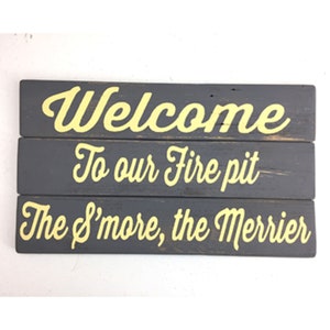 Peut inclure: Panneau rectangulaire en bois gris foncé avec trois planches horizontales. Le texte jaune dit : "Welcome To our Fire pit The S'more, the Merrier."