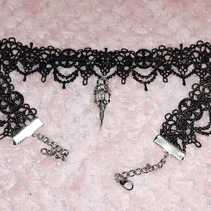 May include: Black lace choker necklace with a silver pendant in the shape of a bird skull.