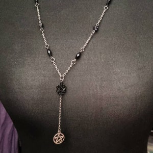 May include: A silver chain necklace with black beads and a pentagram pendant. The necklace also features two crescent moon charms.