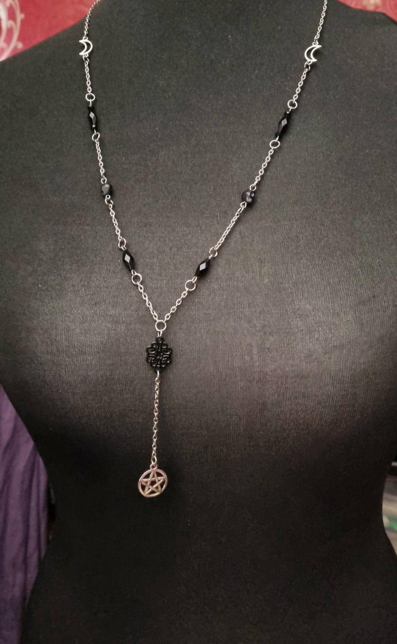 May include: A silver chain necklace with black beads and a pentagram pendant. The necklace also features two crescent moon charms.